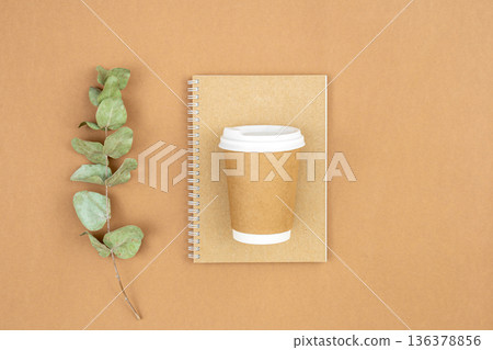 Craft paper coffee cup, notebook and eucalyptus sprig on eco background, flat lay. 136378856