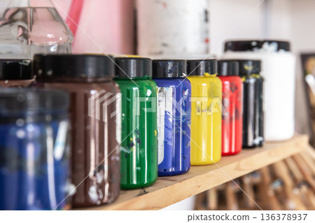 Colored paints for drawing and painting in cans on a shelf in a workshop. Colored paints for drawing and painting in cans on a shelf in a workshop. 136378937