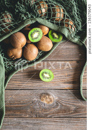 Fruits of kiwi in a mesh bag on a wooden background, top view, rustic style, 136379043