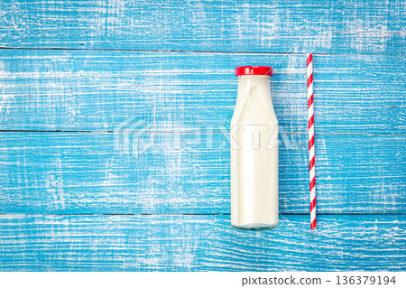 Milk bottle and paper straw on blue wooden background, flat lay. Milk bottle and paper straw on blue wooden background, flat lay. 136379194