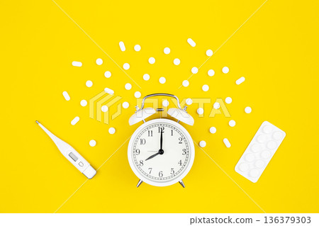 Alarm clock, medical thermometer and pills on a yellow background, flat lay. 136379303