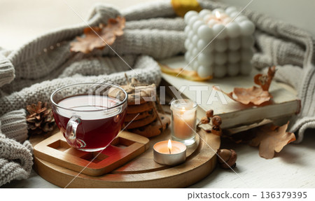 Autumn still life with a cup of tea, candles, cookies and a knitted elements. Autumn still life with a cup of tea, candles, cookies and a knitted elements. 136379395
