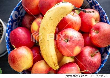 Banana and ripe red apples in a bowl in the kitchen. Banana and ripe red apples in a bowl in the kitchen. 136379426