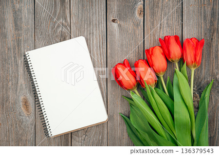 Bouquet of red tulips and notebook on a wooden background, top view. Bouquet of red tulips and notebook on a wooden background, top view. 136379543