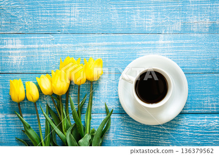 Bouquet of yellow tulips and cup of coffee on a blue background, top view. Bouquet of yellow tulips and cup of coffee on a blue background, top view. 136379562
