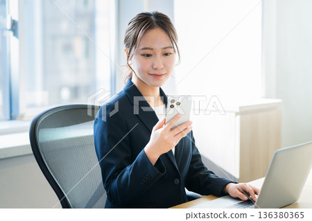 有一部智能手機的女商人在辦公室 有一部智能手機的女商人在辦公室 136380365
