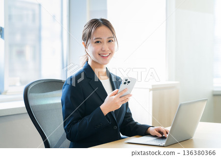 有一部智能手機的女商人在辦公室 有一部智能手機的女商人在辦公室 136380366