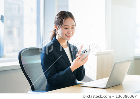 有一部智能手機的女商人在辦公室 有一部智能手機的女商人在辦公室 136380367