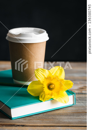 Paper cup, book and yellow flower on a blurred wooden background. Paper cup, book and yellow flower on a blurred wooden background. 136380745