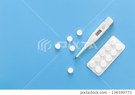 Pills and electronic thermometer on a blue background, flat lay. Pills and electronic thermometer on a blue background, flat lay. 136380773