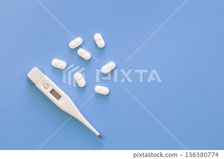 Pills and electronic thermometer on a blue background, flat lay. Pills and electronic thermometer on a blue background, flat lay. 136380774