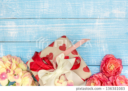 Spring background with flowers and a gift box on a blue background, top view. 136381083