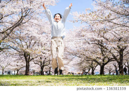 Young woman jumping under a row of cherry blossom trees Lifestyle image Young woman jumping under a row of cherry blossom trees Lifestyle image 136381339