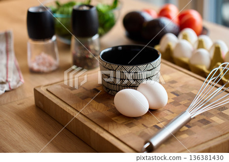 Two Eggs and Whisk on Wooden Cutting Board with Bowl in Kitchen Two Eggs and Whisk on Wooden Cutting Board with Bowl in Kitchen 136381430