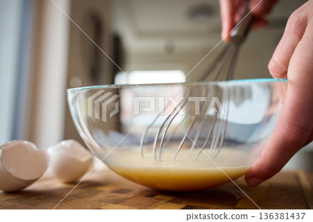 Whisking eggs in glass bowl on kitchen counter during home cooking Whisking eggs in glass bowl on kitchen counter during home cooking 136381437