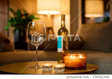 Bottle of white wine, wine glass and candles on table in living room 136381440