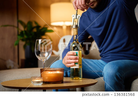 Man opening bottle of white wine with corkscrew at home 136381568