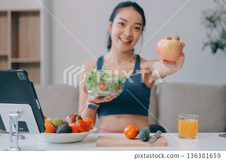 Fit young Asian women in activewear sitting on yoga mat and eating fresh vegetable salad after workout, representing clean eating, fitness lifestyle, wellness routine and health balance. 136381659