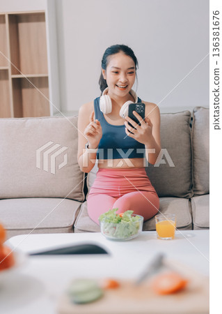 Fit young Asian women in activewear sitting on yoga mat and eating fresh vegetable salad after workout, representing clean eating, fitness lifestyle, wellness routine and health balance. 136381676