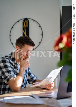 Man reviewing bills and financial documents at home office Man reviewing bills and financial documents at home office 136381844
