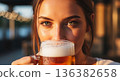 Close-up of a young woman enjoying a refreshing beer with bokeh background. 136382658