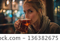 A young blonde woman sips a glass of refreshing beer in a relaxed pub setting. 136382675