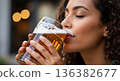 Close-up of a young woman with curly hair drinking a refreshing beer outdoors. 136382677