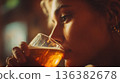 Close-up of a young woman enjoying a golden beer, captured with warm lighting. 136382678