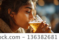 Close-up portrait of a young woman drinking a cold, golden beer with foam, blurred background. 136382681