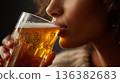 Close-up view of a woman's mouth as she sips refreshing golden beer from a glass. 136382683