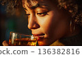 Beautiful woman with curly hair, holding a glass of amber drink. 136382816