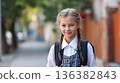 Smiling elementary schoolgirl with braids, wearing uniform and backpack, on a sunny day. 136382843