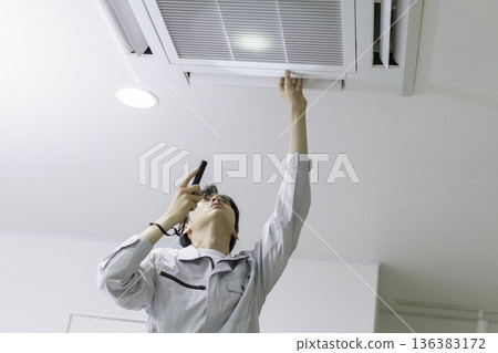 A young Japanese man inspecting a ceiling-mounted air conditioner A young Japanese man inspecting a ceiling-mounted air conditioner 136383172