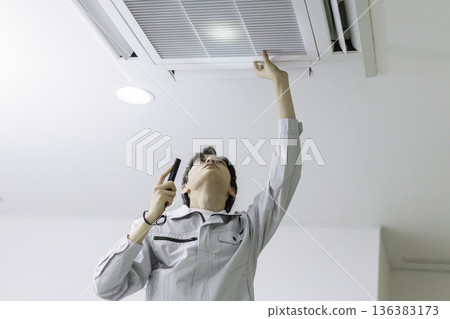 一名年輕的日本男子正在檢查一台天花板空調。 一名年輕的日本男子正在檢查一台天花板空調。 136383173