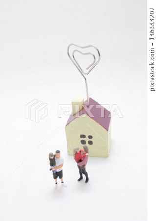 Miniature family gathers beside cute heart topped house 136383202