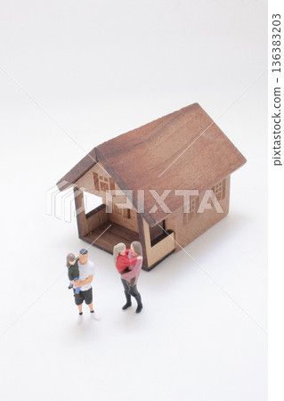 Miniature family stands beside small wooden house model Miniature family stands beside small wooden house model 136383203