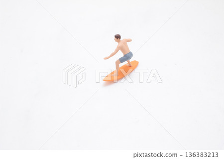 Miniature surfer balances on orange board in studio Miniature surfer balances on orange board in studio 136383213