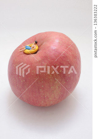 Miniature swimmer relaxes on top of large apple Miniature swimmer relaxes on top of large apple 136383222