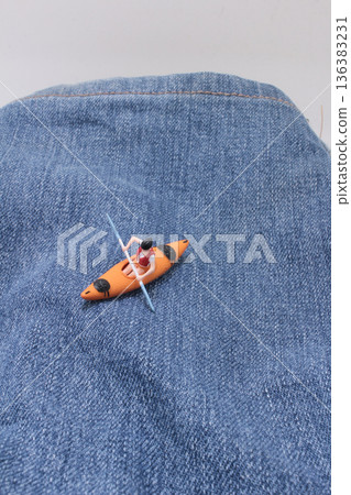 Miniature kayaker paddles across denim fabric landscape 136383231