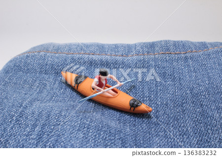 Miniature kayaker paddles across denim fabric landscape Miniature kayaker paddles across denim fabric landscape 136383232