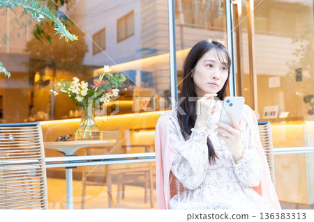 A woman looking at her smartphone on a terrace seat at a cafe A woman looking at her smartphone on a terrace seat at a cafe 136383313