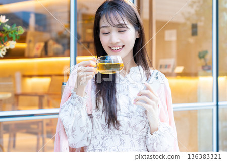 一位女士坐在咖啡館的露台座位上看著她的智慧型手機。 一位女士坐在咖啡館的露台座位上看著她的智慧型手機。 136383321