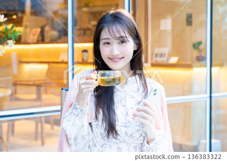 一位女士坐在咖啡館的露台座位上看著她的智慧型手機。 一位女士坐在咖啡館的露台座位上看著她的智慧型手機。 136383322