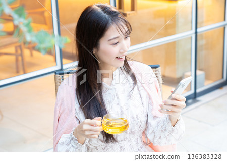 一位女士坐在咖啡館的露台座位上看著她的智慧型手機。 一位女士坐在咖啡館的露台座位上看著她的智慧型手機。 136383328