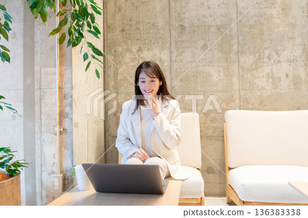 A young woman sitting on a sofa in a cafe and having a remote meeting on a computer 136383338