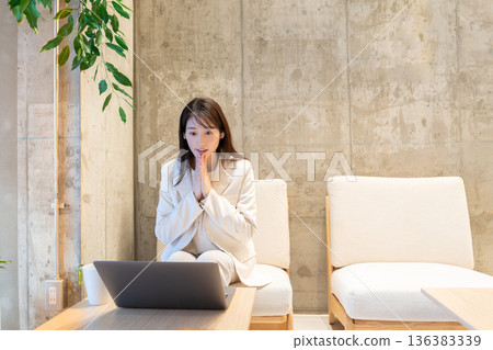 A young woman sitting on a sofa in a cafe and having a remote meeting on a computer 136383339