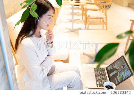 A young woman sitting on a sofa in a cafe and having a remote meeting on a computer A young woman sitting on a sofa in a cafe and having a remote meeting on a computer 136383343