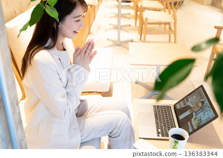 A young woman sitting on a sofa in a cafe and having a remote meeting on a computer A young woman sitting on a sofa in a cafe and having a remote meeting on a computer 136383344