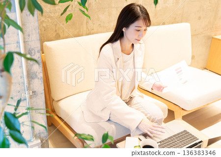 A young woman sitting on a sofa in a cafe and having a remote meeting on a computer 136383346