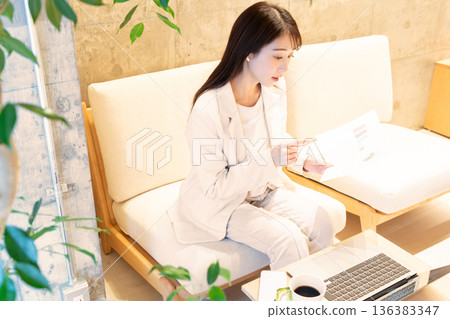 A young woman sitting on a sofa in a cafe and having a remote meeting on a computer A young woman sitting on a sofa in a cafe and having a remote meeting on a computer 136383347